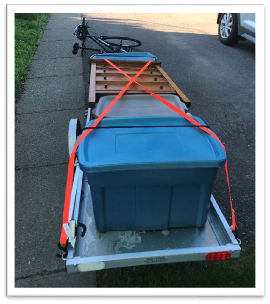 rear view of trailer loaded with plastic bins and a clothes dresser, all secured by ratchet straps